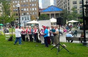 15 singers in white shirts and red choir stoles gathered outdoors at the Boston Common to sing for peace